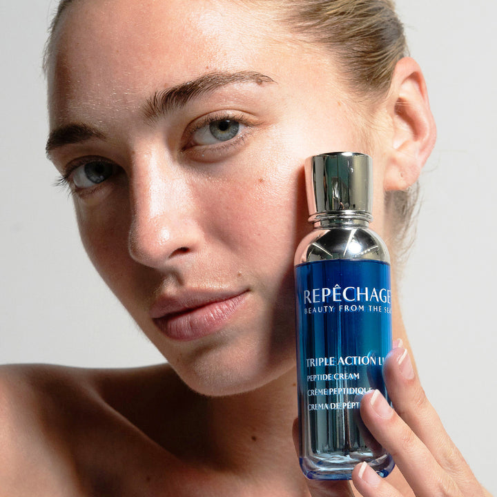 Person holding a Repèchage skincare bottle close to their face against a neutral background