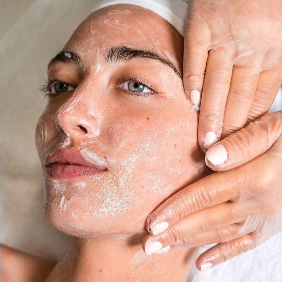 Woman receiving a facial treatment with hands applying product to her face.