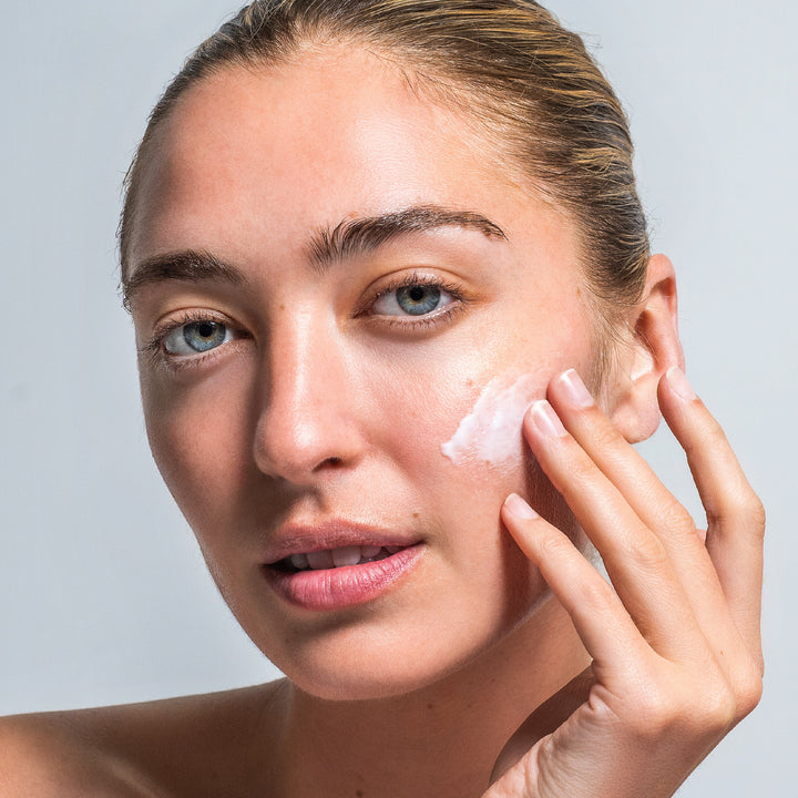 Woman with hands applying product to her face.