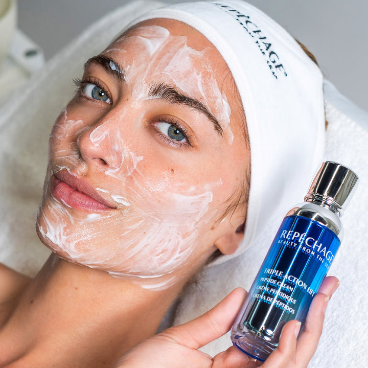 Woman with a face mask holding a Repechage skincare product.